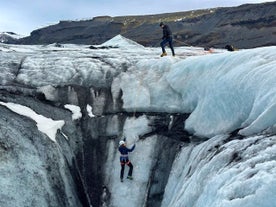 Twee mensen zijn aan het ijsklimmen op de Solheimajokull-gletsjer met de bergen op de achtergrond.