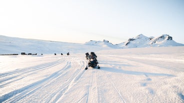 A group rides snowmobiles across the snowy Eyjafjallajokull glacier in Iceland during a winter adventure tour.