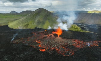 Eruption of Fagradalsfjall volcano in Iceland with glowing lava and smoke rising against green mossy hills.