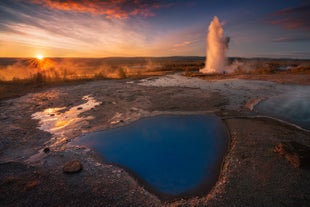 De Strokkur-geiser barst uit naast een stomende warmwaterbron in de Haukadalur-vallei in IJsland tijdens een kleurrijke zonsondergang.