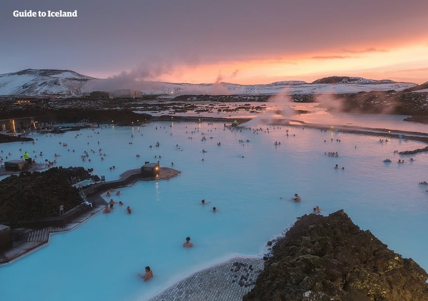 Blue Lagoon geothermal spa in Iceland at sunset with people bathing in milky blue water surrounded by lava fields and steam